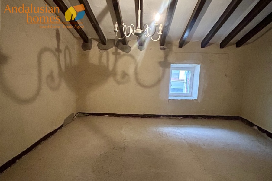Rear bedroom with beamed sloping ceiling with window looking over patio and terrace