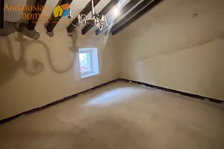 Rear bedroom with beamed sloping ceiling with window looking over patio and terrace